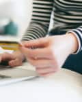 Person in striped shirt using a laptop and holding a credit card.