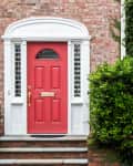 Red and white front doors side by side, surrounded by brick and ivy-covered walls, with a green bush in between.