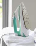 Iron on ironing board next to folded clothes, with a green plant in the background.