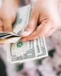Hands counting a stack of US dollar bills.