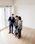 Real estate agent showing an empty room with wooden floors to a family of three.