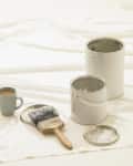 Two open paint cans, a large paintbrush, and a mug of coffee on a white sheet.