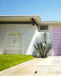 Mid-century modern house with a pink door, agave plants, and manicured lawn under a clear blue sky.