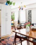 Stacked washer and dryer next to stainless steel fridge in a bright dining area with a wooden table and colorful decor.