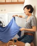 Mother and daughter folding a blue towel in a laundry room with a washing machine.