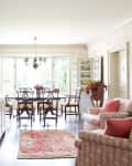 Spacious kitchen with island, dining table, pink armchairs, floral rug, and large windows.