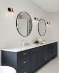 Bathroom with dark blue double vanity, marble countertop, round mirrors, and wall sconces, leading to a walk-in closet.