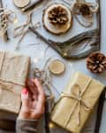 Hands Holding Gift By Christmas Decorations On Table