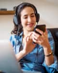Happy young woman wearing headphones selecting a music playlist while working on laptop.