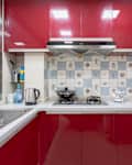 Modern kitchen with red cabinets, patterned backsplash, stainless steel sink, kettle, blender, and gas stove.