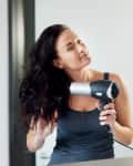 woman blowdrying her hair in front of a mirror in the bathroom