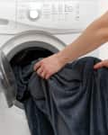 Woman hands put laundry into the white washing machine. She standing inside bright apartment with light interior