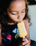 Girl eating popsicle while sitting on bed at home