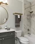Bathroom with round mirror, marble tiles, gray vanity, and gold fixtures.