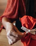 Person wraps presents in reusable homemade fabric wrap and ribbon with Christmas tree and gifts in the background