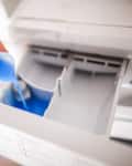 Someone pouring liquid detergent into laundry machine.