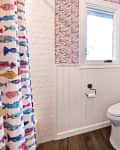 Bathroom with colorful fish-patterned wallpaper, white wainscoting, a toilet, and a towel hanging on the wall.