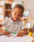 african american toddler drawing using paper and marker pen at kindergarten