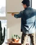 Rare view of a young man doing DIY project at home using measuring tape.