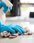 Someone cleaning the floor with a cloth wearing blue rubber gloves
