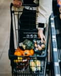 Close up of woman's hand shopping for fresh groceries in supermarket and putting a variety of organic vegetables in shopping cart