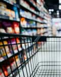 Personal perspective of a shopper pushing shopping trolley along product aisle while shopping in a supermarket