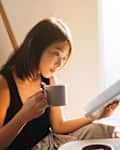 Young Woman Reading Book While Drinking Coffee