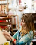 Woman browsing items in a vintage shop, surrounded by eclectic decor and furniture.
