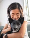 Young woman hugging dog on living room sofa