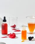 Skincare serums in glass bottles with droppers, surrounded by beakers and red flower petals.