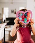 Young girl standing inside with rainbow heart in hands
