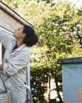 Woman repairing the outdoor window trim on her house