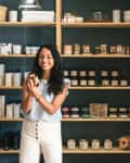 woman reading label on candle in store. There are shelves behind her with many more candles and other small household goods