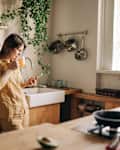 Beautiful mature woman talking on the phone in living-room, drinking coffee and having breakfast