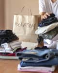 Person with stacks of clothes on a table, sorting them to donate