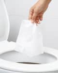 Close up hand holding a tissue to be thrown into the toilet bowl.