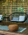 Terrace house with plants, wooden wall and table, comfortable sofa, armchair and lanterns. Cozy space in patio or balcony. Wooden veranda with garden furniture. Modern lounge outdoors in backyard