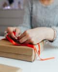 woman wearing gray fuzzy sweater wrapping a gift with red ribbon
