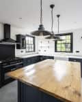 Expansive view of granite countertops, cement floor, kitchen island, pendant lights, black accented cabinets and appliances, and access to outdoor patio.