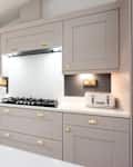 An interior view of a taupe, champagne coloured shaker style fitted kitchen diner with gold handles, quartz island, gas cooker hob, toaster