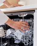 A white woman with long hair in purple pants and white blouse puts crockery to wash in the dishwasher