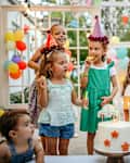 Children with cake standing around table on birthday party in garden in summer.