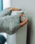Cropped female hands in warm sweater trying to keep warm near battery radiator. Cold temperature