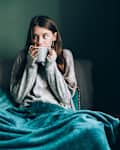 Young woman drink hot tea, wrapped in blanket in cold apartment