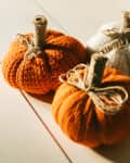 Decorative knitted pumpkins from white and orange threads. Handmade. Halloween and Thanksgiving Day zero waste concept. DIY decor. Hard shadows from sunlight