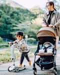 Girl with sunglasses riding a scooter with her mother pushing a baby stroller
