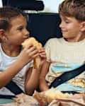 Brother and sisters in the backseat of their family car eating snacks