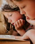 Two children lie on their tummies and read the same book together