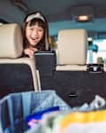 Lovely cheerful girl in back seat looking at the car trunk which full of shopping bags with excitement. She is getting ready for the road trip with her family.