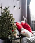 Small christmas tree on the bedside table and gifts near the bed in stylish bedroom